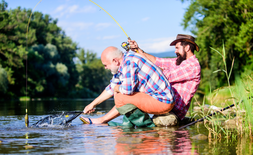 Männer sitzen mit Angelausrüstung am Flussufer. Wilderei Verbrechen und Fischereilizenz. Wilderer fischen. Kaviar vom Schwarzmarkt. Illegale Jagd auf Kaviar. Extrahiert Eier von Stören, die im Fluss gefangen wurden. Falle für Fische